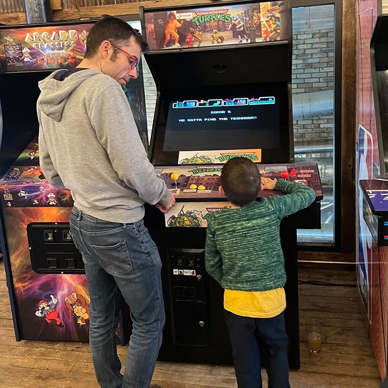 A member of the Factory speaking with a child while standing in front of a video game machine.
